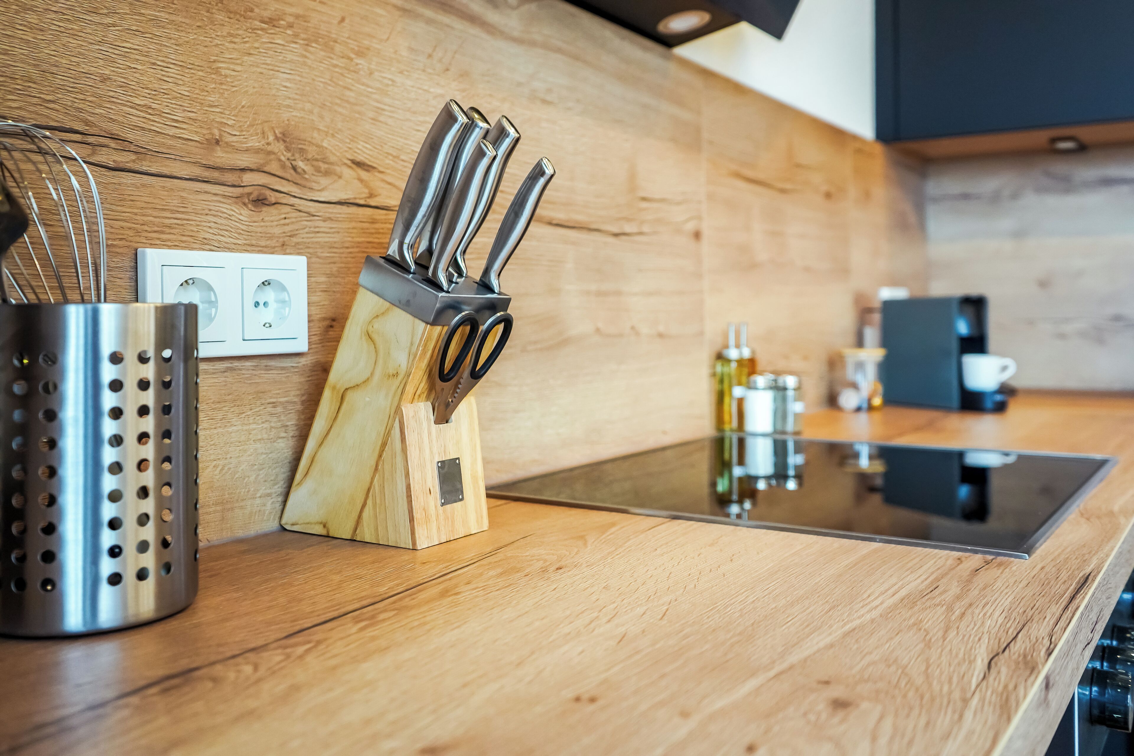 Una cocina moderna con encimera de madera, un bloque de cuchillos empotrado, un colador de acero inoxidable y una máquina de café.