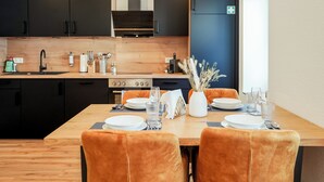 Eine moderne Küche mit dunklen Schränken, einer Holzarbeitsplatte und einem Essbereich mit orangefarbenen Stühlen und einem für vier Personen gedeckten Holztisch.