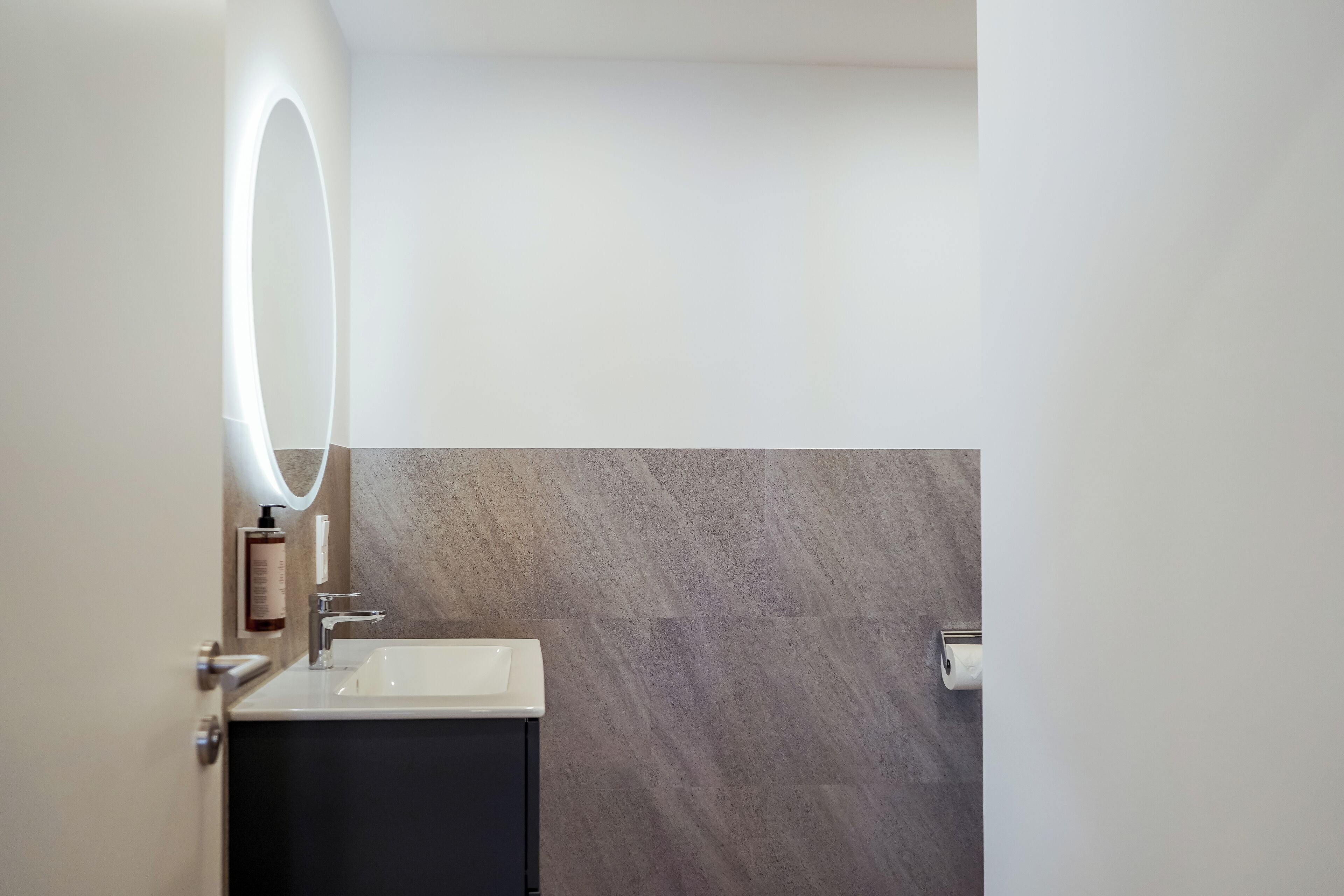 Une salle de bain moderne avec un lavabo blanc, un meuble sombre et un miroir fixé au mur, agrémenté d’un éclairage.