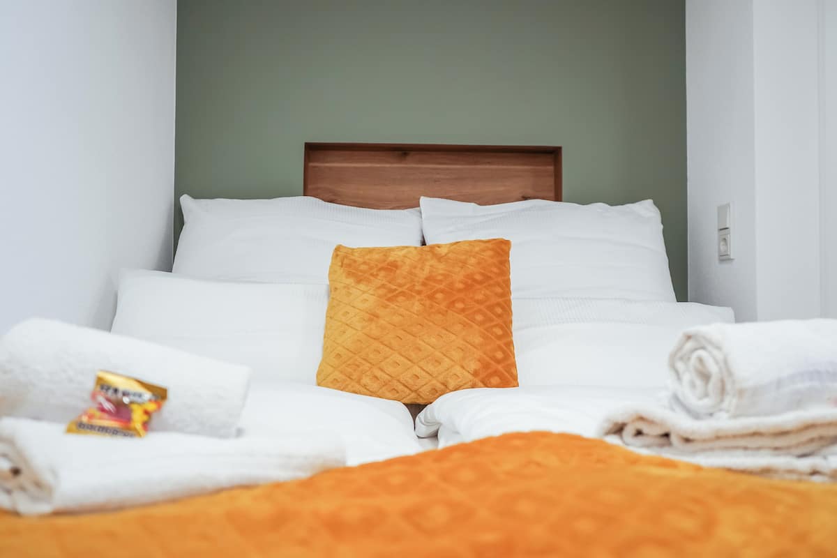 A neatly made bed with white and orange bedding, a wooden headboard, and a green wall.