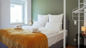 Ein Hotelzimmer mit Bett, Fenster, Nachttisch mit Lampe und einer Wandregal.
