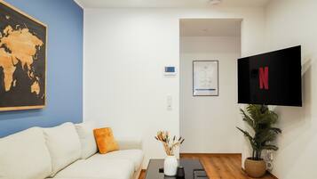 A modern living room with a white sofa, a black coffee table, a world map painting, a plant, and a TV displaying the Netflix logo.