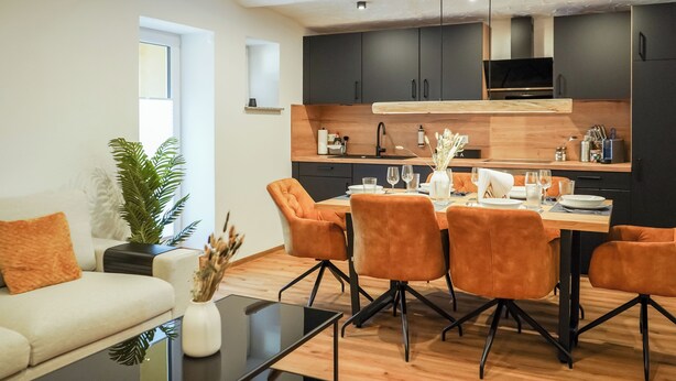 Eine moderne Küche mit dunklen Schränken, einem Holztisch und orangefarbenen Stühlen.