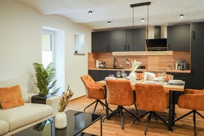 Una cocina moderna con armarios oscuros, una mesa de comedor de madera y sillas naranjas.
