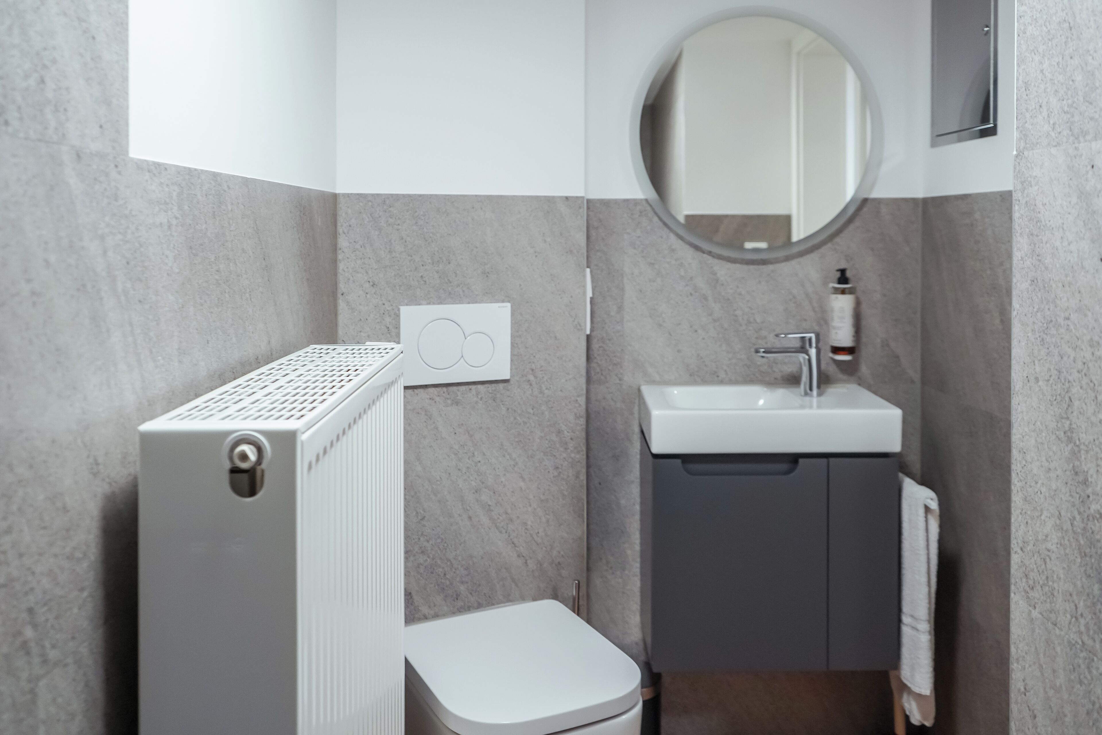 Un bagno moderno con un water bianco, un lavandino grigio e uno specchio rotondo.