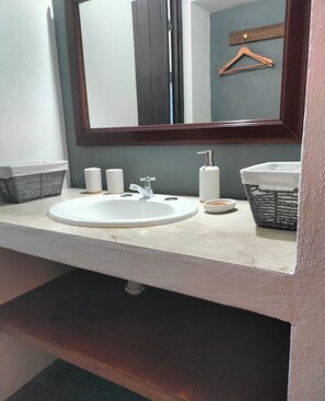 A bathroom with a white sink and mirror, featuring a dark wood frame, and a convenient storage basket.