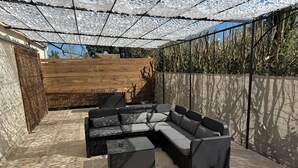 Ein Sitzbereich im Freien mit einer Eckcouch und Stühlen, einer Pergola darüber und einem Holzzaun im Hintergrund.