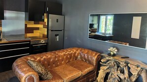 Eine moderne Küche mit einem Edelstahl-Kühlschrank, einer Holz-Spritzschutzleiste und einem Ledersofa in einem Wohnbereich mit einem großen Spiegel und einem Holztisch.