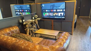 Ein modernes Wohnzimmer mit einer Ledersofa, einem Holztisch und einem großen Flachbildfernseher, der an einer Holzverkleidung angebracht ist.