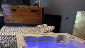 Ein modernes Schlafzimmer mit einem Holzkoffer, einem bettenartig gemusterten Bett und einer Badewanne mit blauer Beleuchtung.