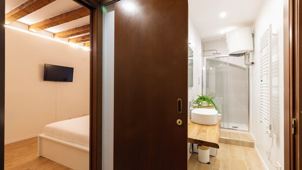 Un dormitorio con cama, televisor montado en la pared y techo de madera.