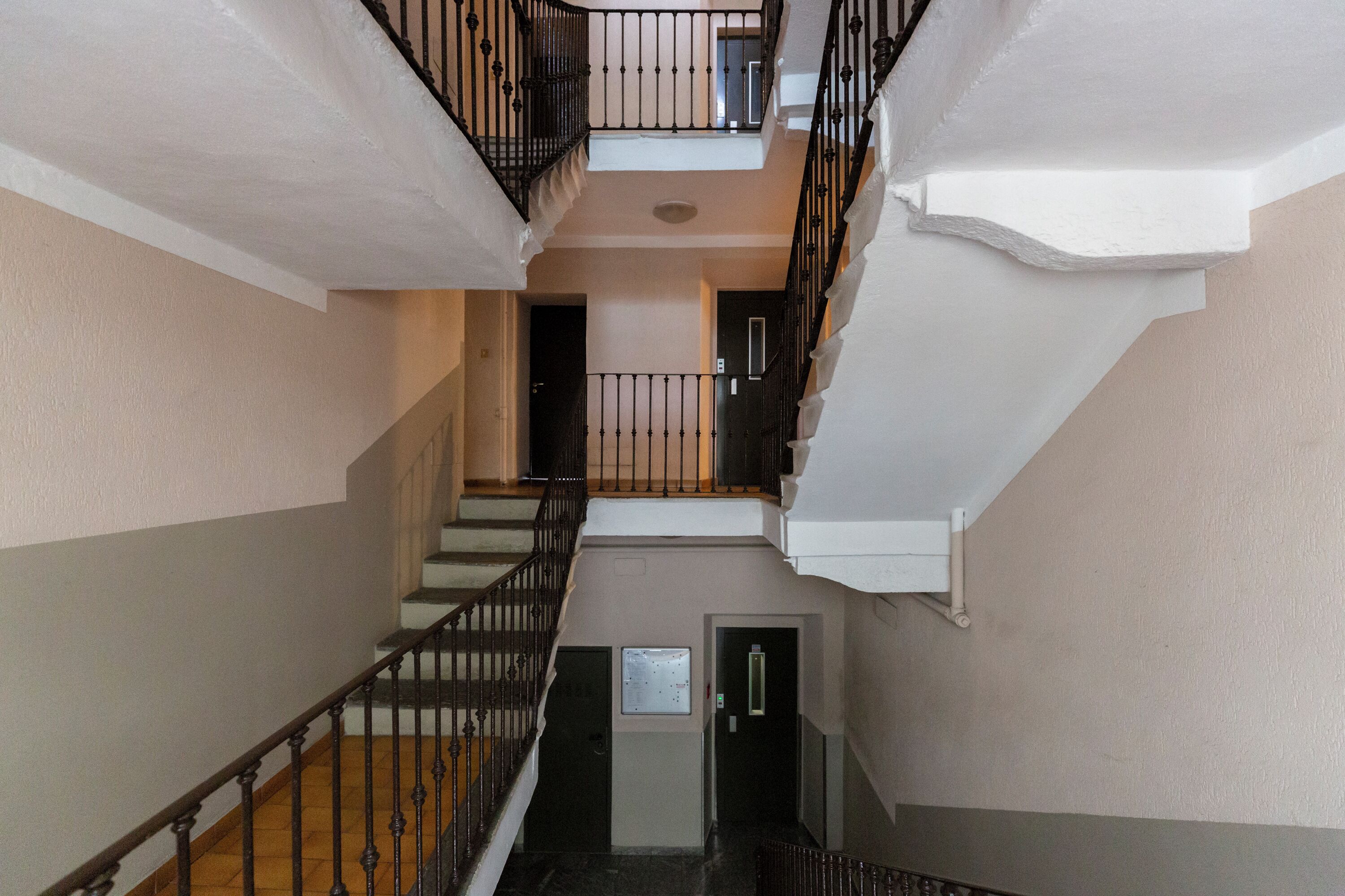 Interior de varios niveles con una escalera, barandillas negras y una puerta con un letrero.