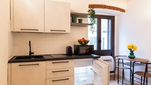 Una cocina compacta con armarios blancos, encimera negra y microondas integrado. Hay una ventana con vistas a la ciudad y un pequeño comedor con mesa y sillas.