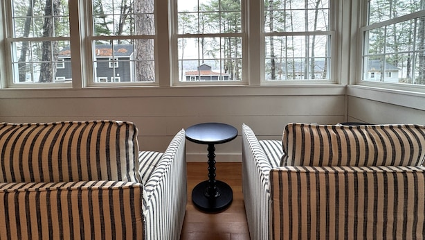Une pièce dotée d’une grande baie vitrée, de deux fauteuils à rayures et d’une petite table ronde.