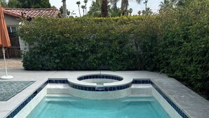 A rectangular swimming pool with a circular hot tub in the center, surrounded by a tiled deck and lush greenery. - Charming 3-bedroom house with AC and WiFi in Palm Springs (Palm Springs)