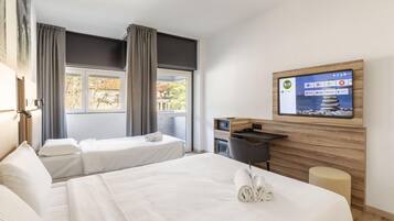 Ein Hotelzimmer mit zwei Betten, einem Schreibtisch, einem an der Wand montierten Fernseher und einem Fenster mit Vorhängen.