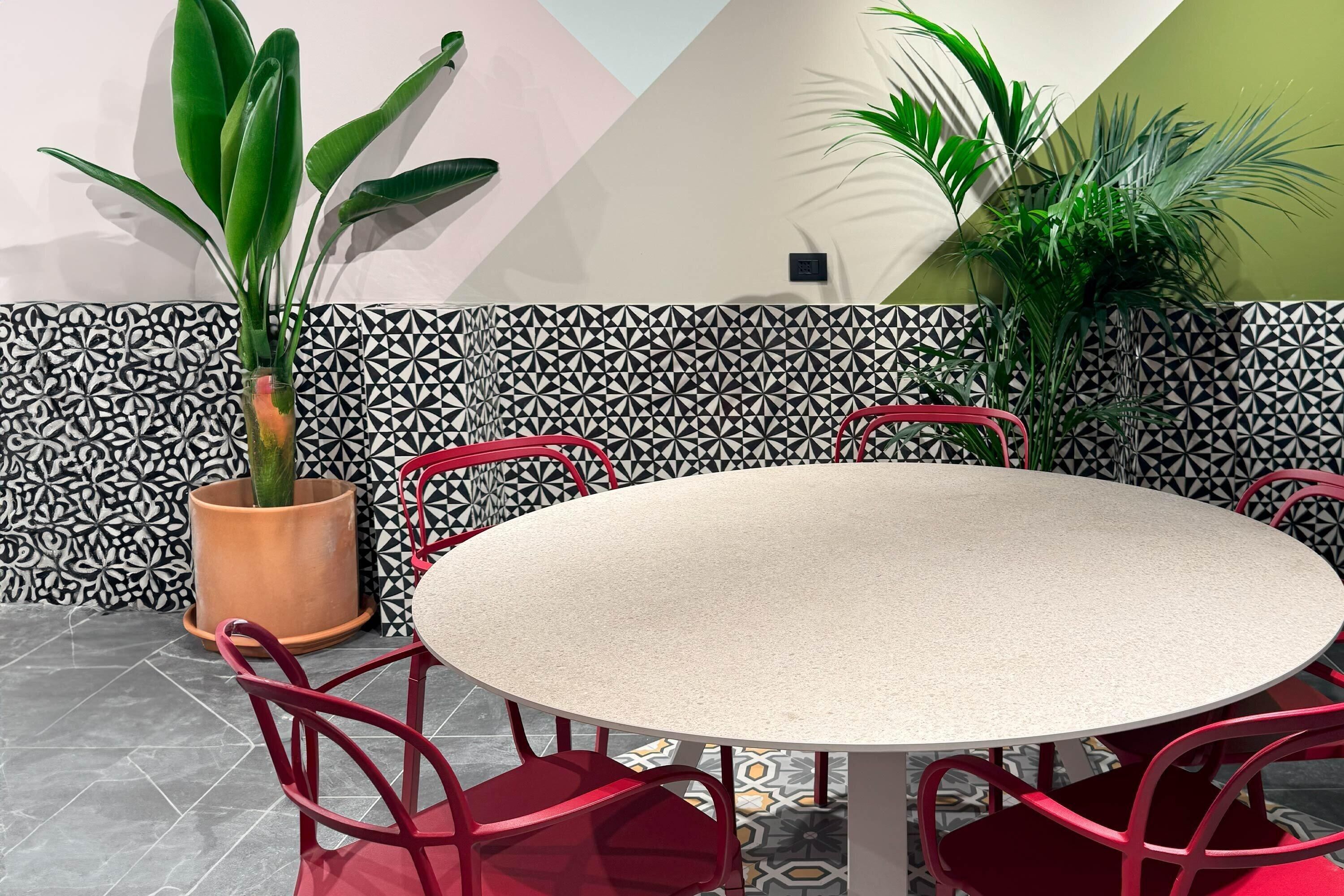 Une table ronde entourée de six chaises rouges, le tout agrémenté de carreaux décoratifs et de plantes en pot.