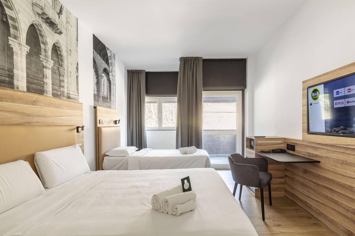 Quarto de hotel com duas camas, uma mesa e uma televisão exibindo serviços de streaming.