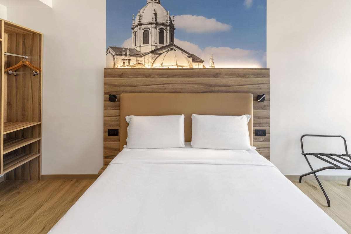 Quarto com uma cama, um guarda-roupa de madeira e um porta-casacos fixado na parede.