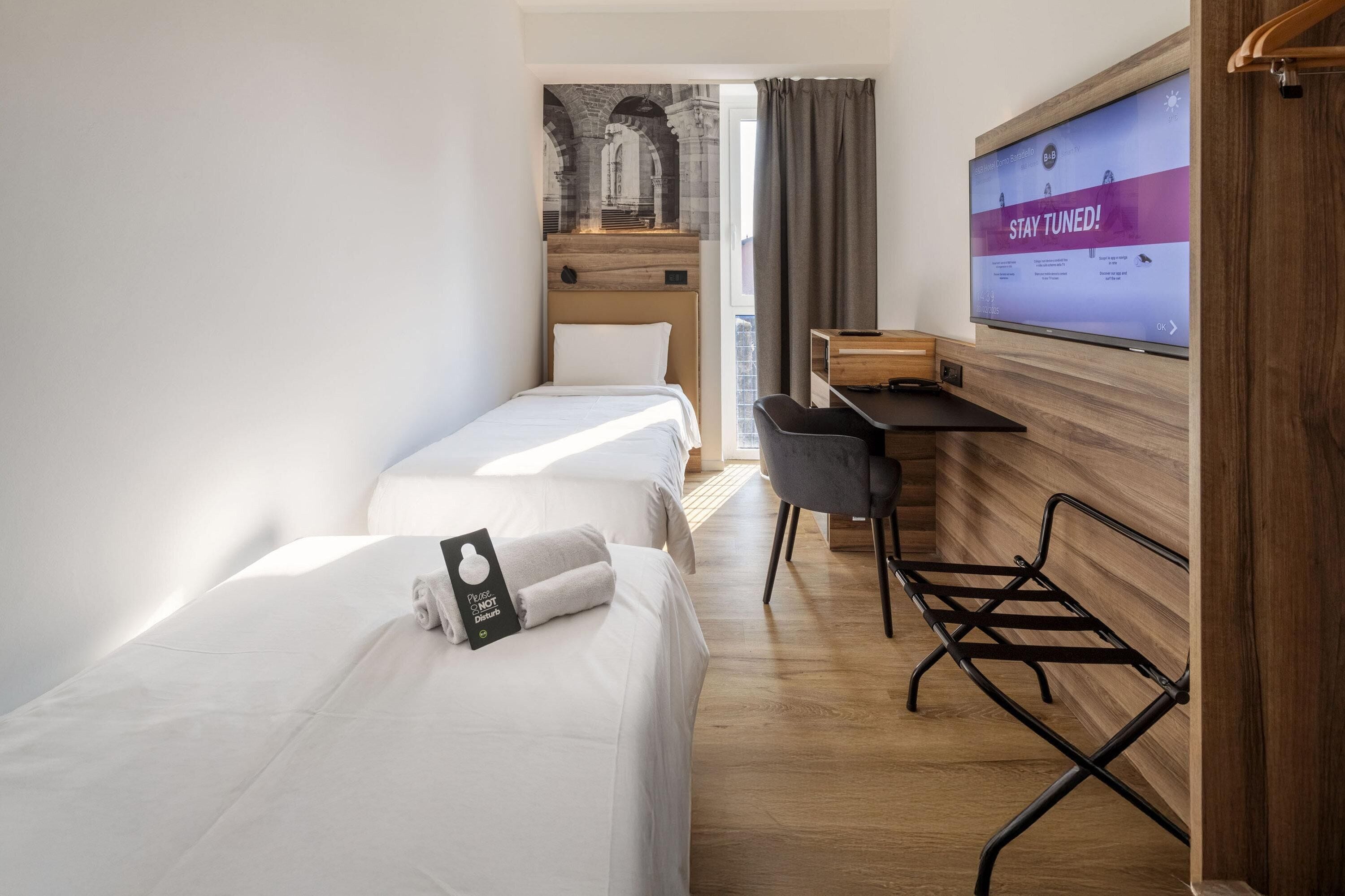 Habitación de hotel con dos camas, un escritorio, un televisor y vistas a un espacio exterior.
