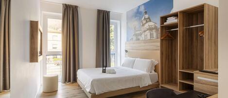 Habitación de hotel moderna con una cama grande, un armario de madera, una mesita y vistas a un edificio a través de la ventana.