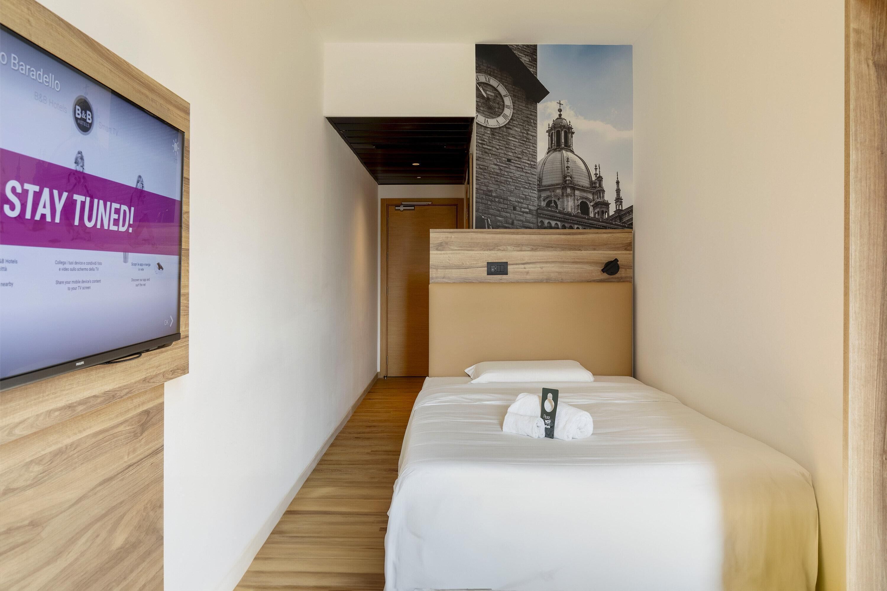 Una habitación de hotel con una cama, un televisor mostrando un mensaje y un cartel de un edificio.