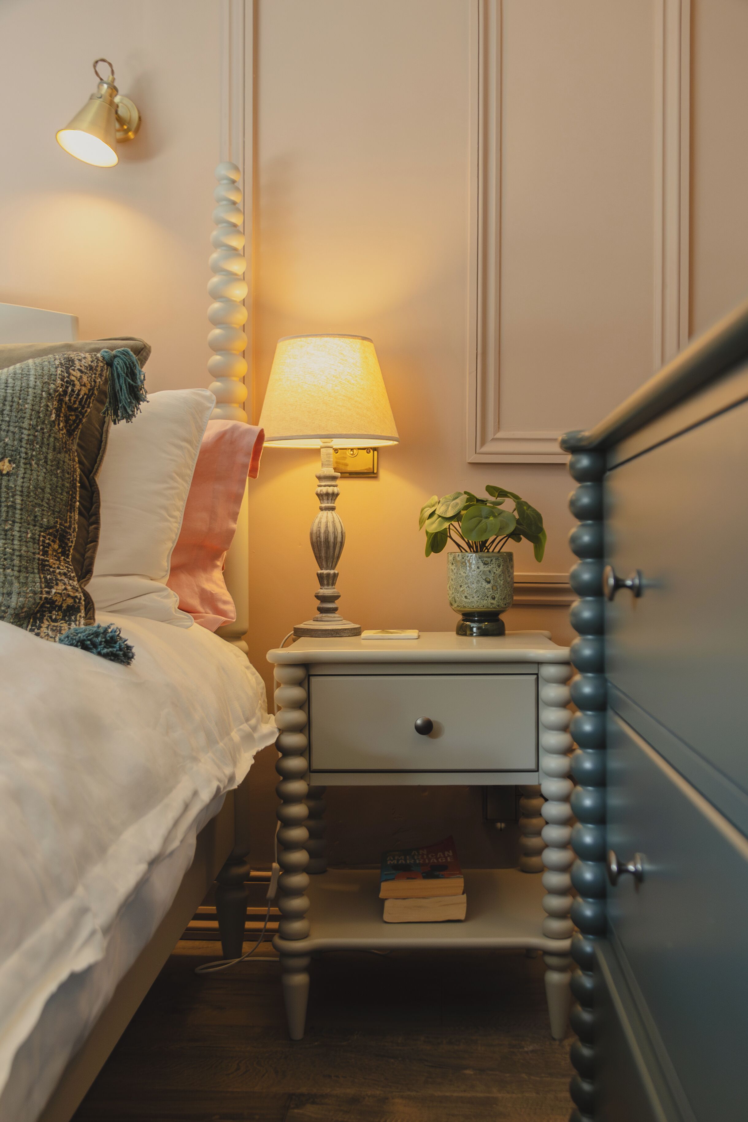A neatly made bed with a lamp and a plant beside it.