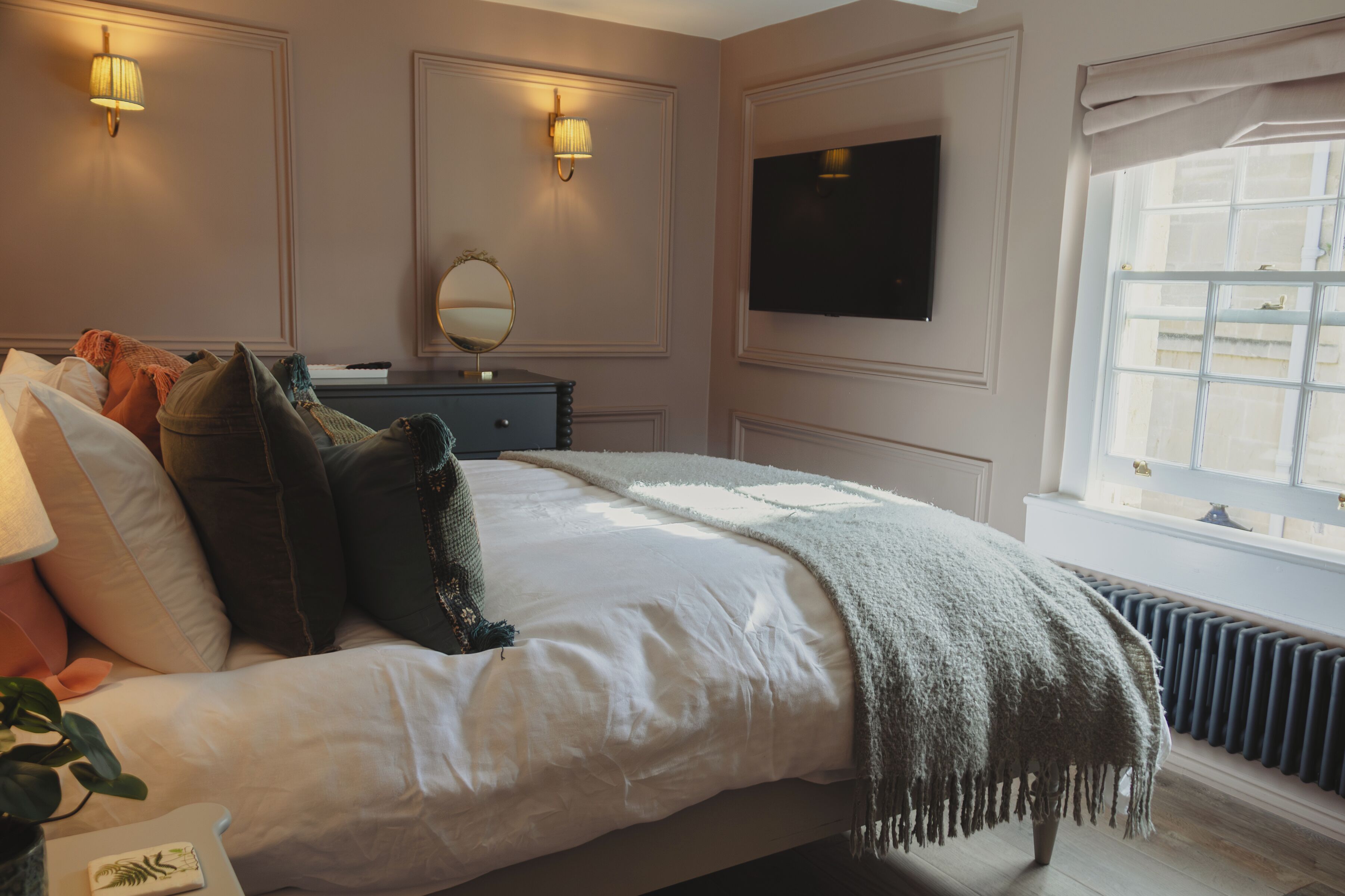 Een slaapkamer met een groot bed, nachtlampjes, een spiegel, een televisie en een raam met uitzicht.