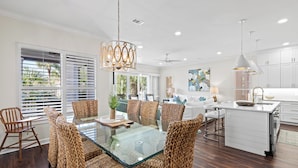 A modern kitchen with white cabinets, a glass island, and a dining area with wicker chairs and a glass table. - Across from Community Pool and Hot Tub, Close to Beach, Gated Community (Destin)