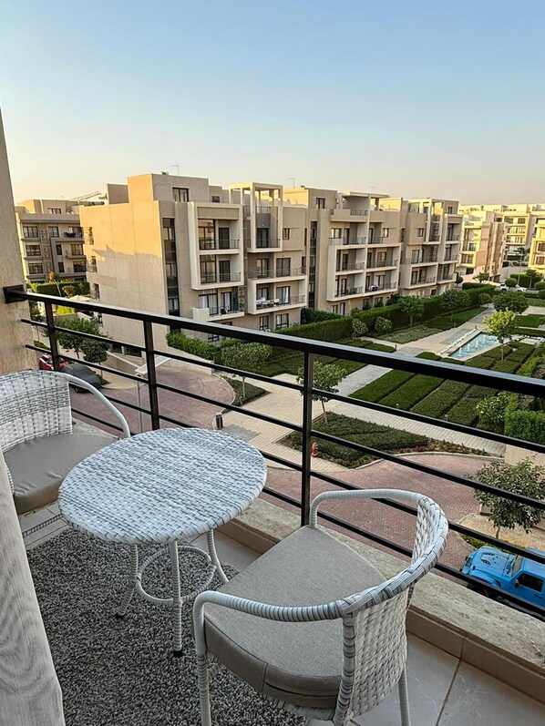A balcony with wicker furniture, a view of modern apartment buildings, and a landscaped garden. - Spacious 3-bedroom apartment with AC and WiFi in charming Fifth Square AlMarasem (Fifth Square Al Marasem)
