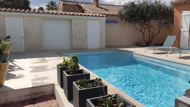Une piscine dont le fond est recouvert de carrelage, entourée de plantes en pot et de chaises longues.