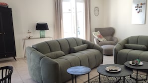 Un salon avec deux canapés verts, une petite table, un meuble et un mur orné d’un masque décoratif.