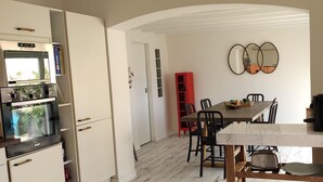 Une cuisine équipée d’un four encastré, un coin repas avec une table et des chaises, et un meuble rouge.