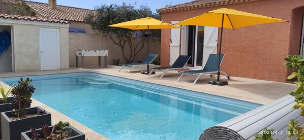 A swimming pool with lounge chairs and yellow umbrellas, surrounded by a building with a tiled roof and a door.