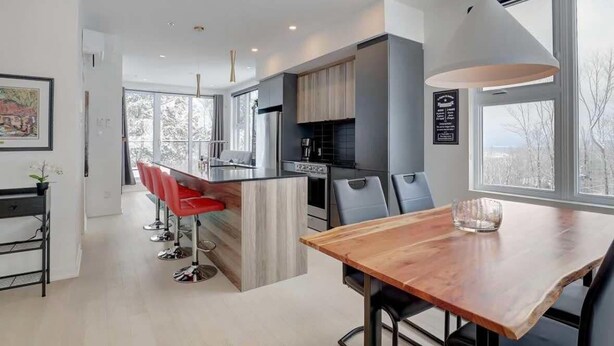 Una cocina moderna con una isla central, taburetes rojos y una mesa de comedor con sillas.