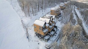 Una hilera de edificios modernos de varios pisos, un paisaje cubierto de nieve y un área boscosa a la derecha.