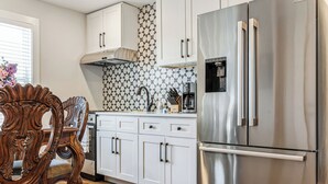 A kitchen with white cabinets, a stainless steel refrigerator, and a patterned backsplash. - Regal Retreat with City Views (Raleigh)