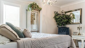 A bedroom with a bed, a dresser, a mirror, and a potted plant. - Regal Retreat with City Views (Raleigh)