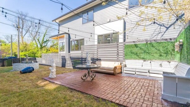 A modern house with a patio area featuring a table and chairs, a stone fireplace, and a green wall. - Regal Retreat with City Views (Raleigh)