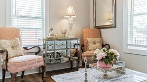 A room with two vintage-style chairs, a marble coffee table with decorative items, a sideboard with a lamp, and a mirror on the wall. - Regal Retreat with City Views (Raleigh)