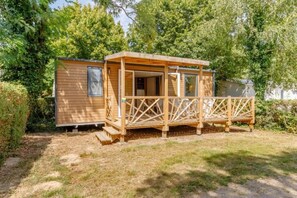 Eine Holzhütte mit Veranda und einem kleinen Anbau, umgeben von Bäumen.