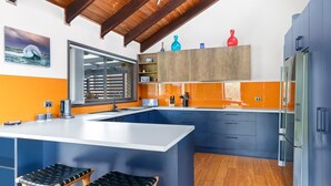 A modern kitchen with a large island, blue cabinets, orange backsplash, and a wooden ceiling. - 93 Montague Ave Kianga (Kianga)