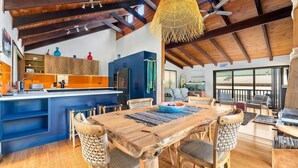 A spacious living area with a wooden dining table, wicker chairs, and a large window offering a view of the outdoors. - 93 Montague Ave Kianga (Kianga)