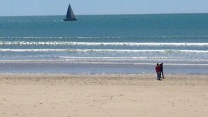 Ein Strand mit einem Segelboot in der Ferne und einer Person, die am Sand steht.