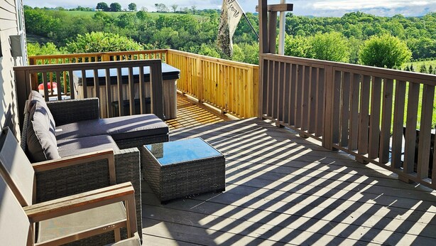 Une terrasse extérieure couverte offrant une vue sur un paysage verdoyant, avec un drapeau et du mobilier d’extérieur.