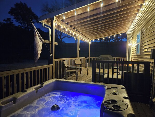 Ein Whirlpool mit blauem Licht, eine Holzterrasse, Gartenmöbel und Lichterketten.
