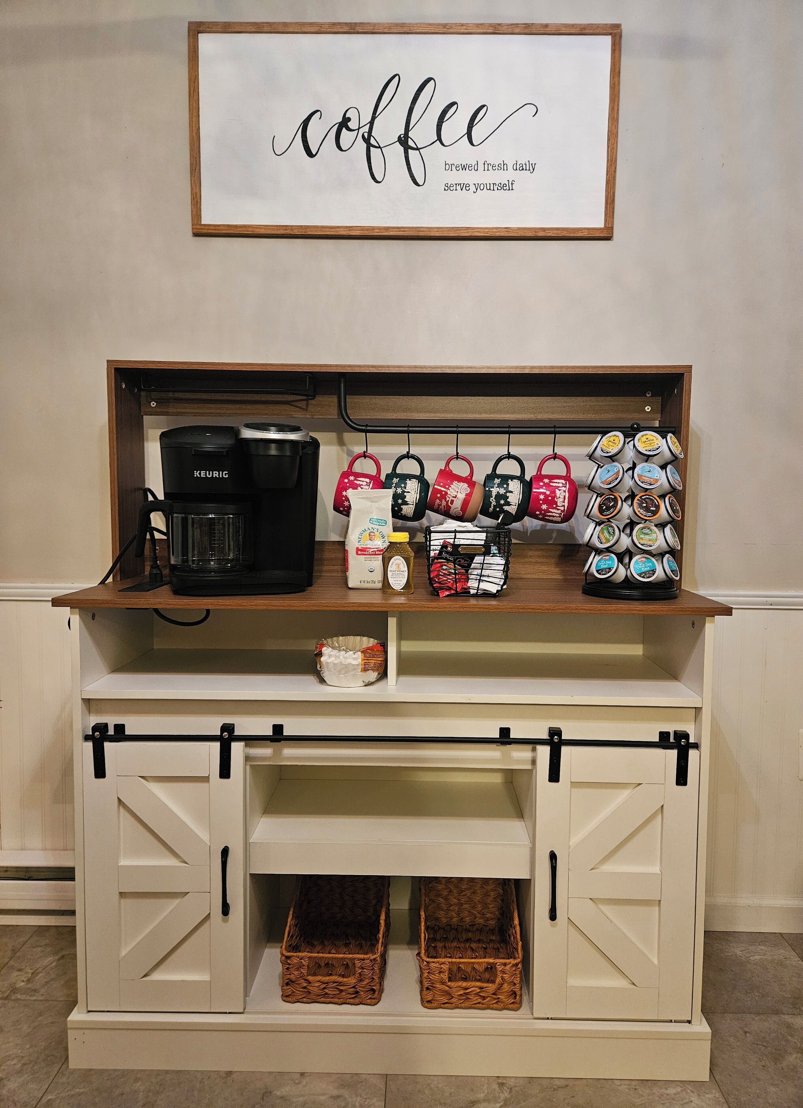 Una zona de cafè amb una màquina de cafè Keurig, càpsules de cafè, tasses i un cartell amb temàtica de cafè a la paret.
