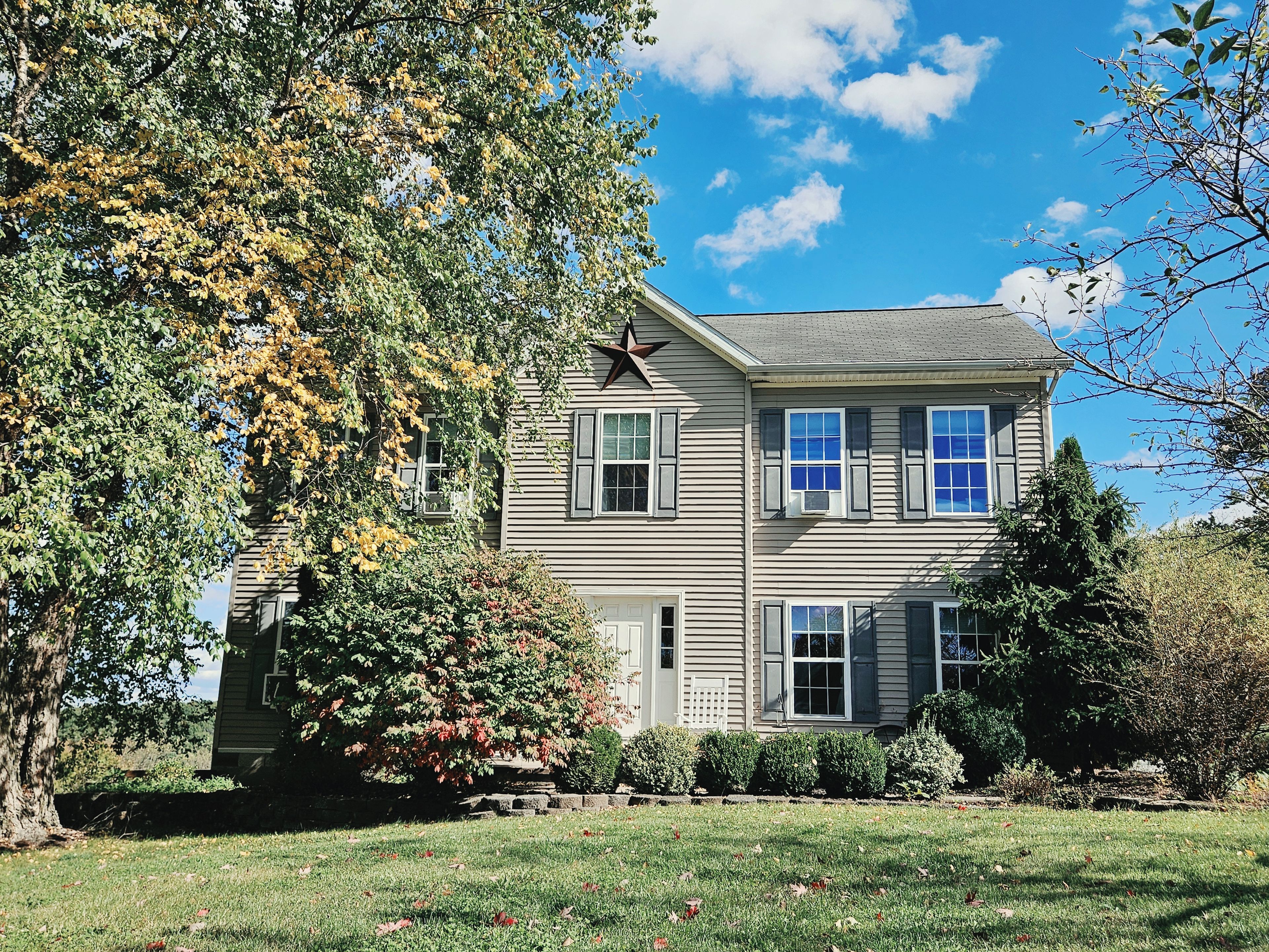 A two-story house with a star on the roof, surrounded by trees and a well-maintained lawn.