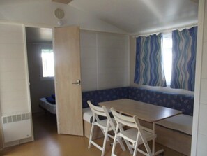 A compact room with a kitchenette, a dining area with a table and chairs, and a window with curtains.