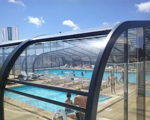 A covered swimming pool with clear skies and a few people in the water.